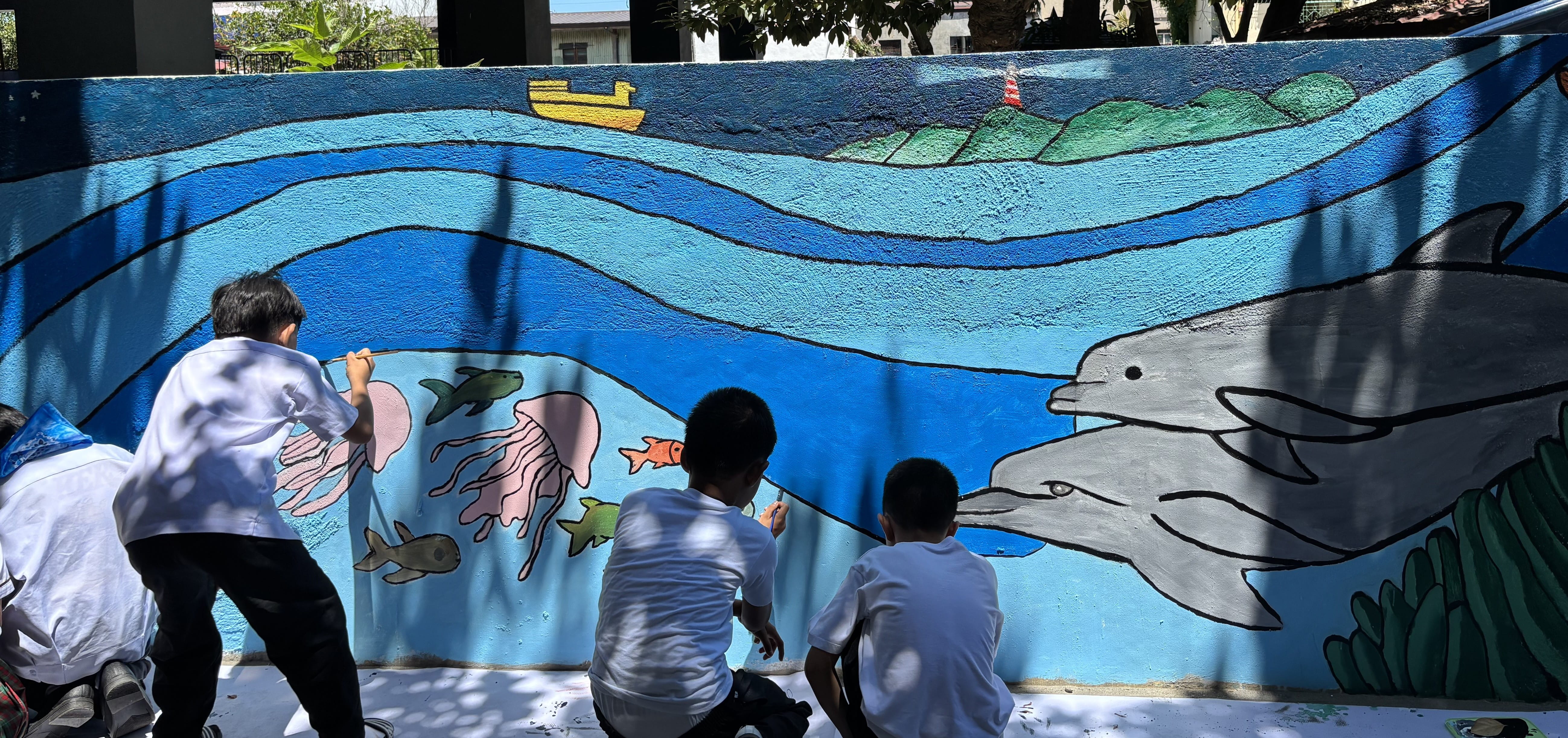 Children painting dolphins and jellyfish on a blue section of the mural depicting the deep sea.